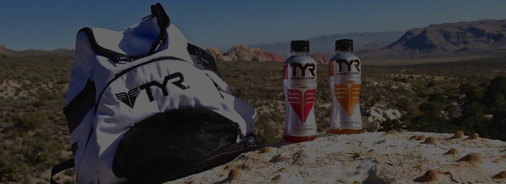 Tyr drinks sitting on a rock overlooking a vista with a Tyr-branded backpack nearby